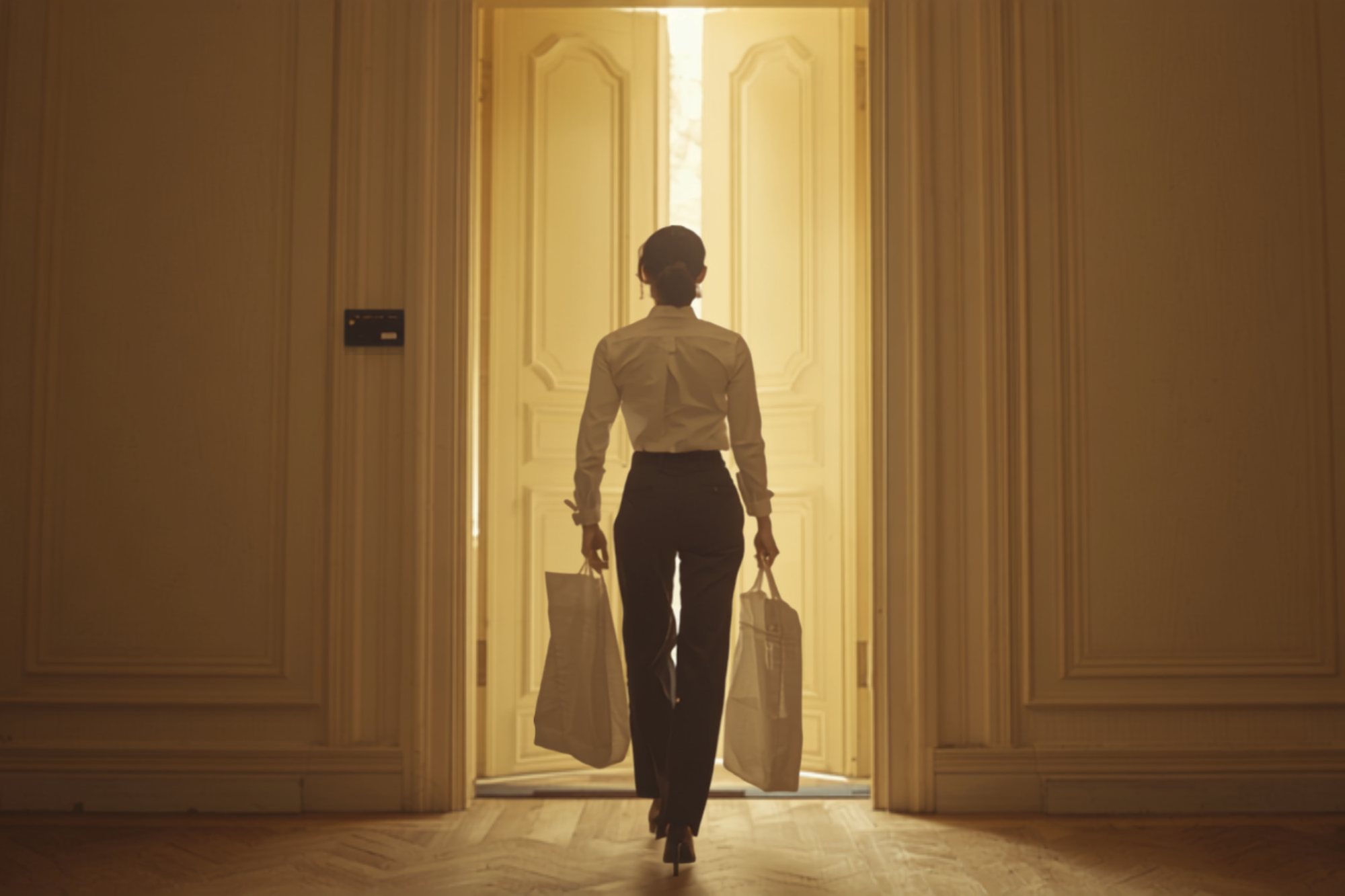 A concierge handing a pale linen garment bag to a client at an elegant doorway in late-afternoon light